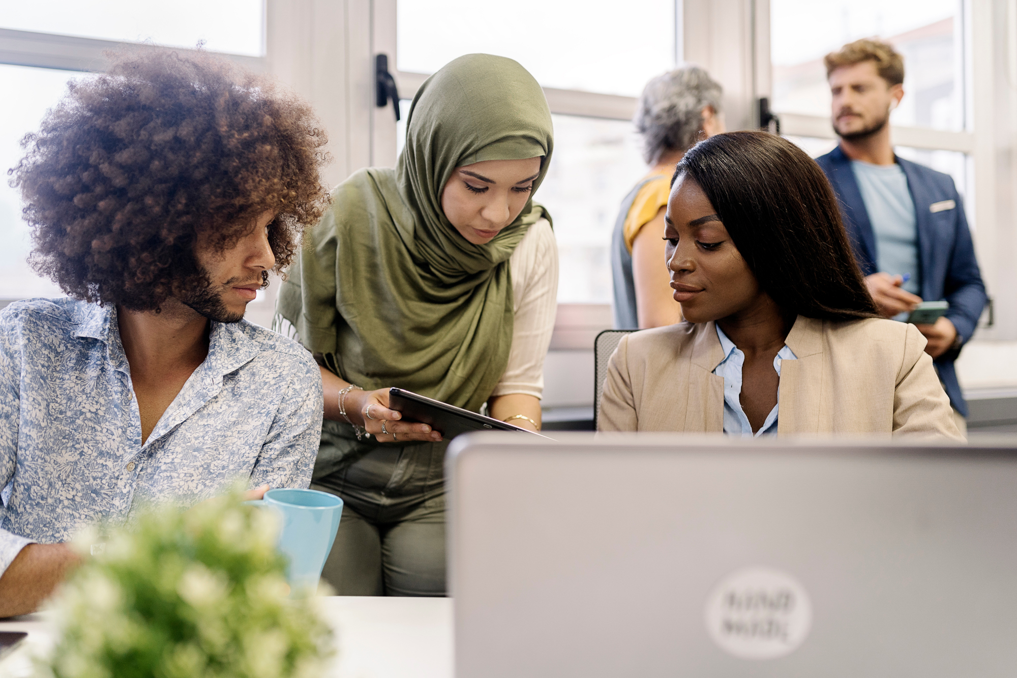 multinational team concept. muslim woman in hijab, a african woman and curly hair man working together in the office using laptop. Coworking concept