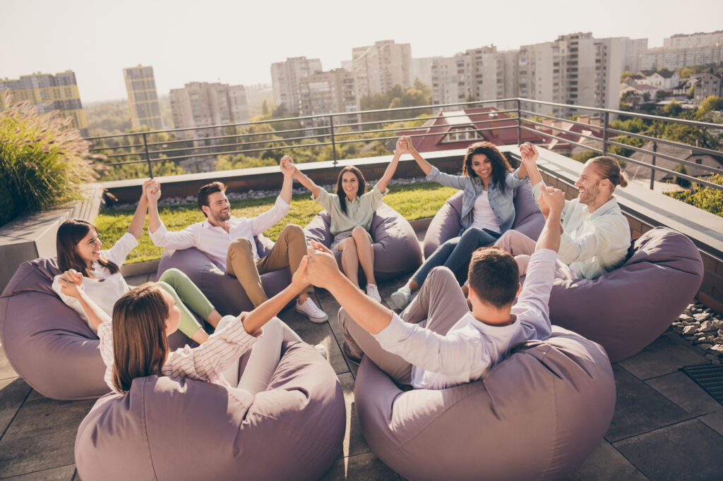 Photo of happy agents sitting beanbags corporate trust training rising arms workplace workstation outdoors outside urban terrace.